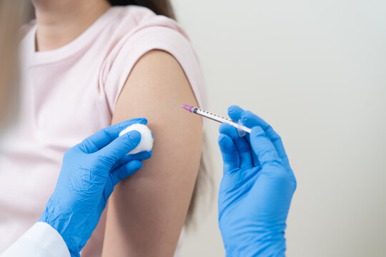 Close up of doctor in blue gloves giving vaccine injection to a female patient.