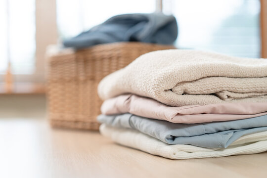 A neat stack of clean folded clothes on wooden table with wicker laundry basket.