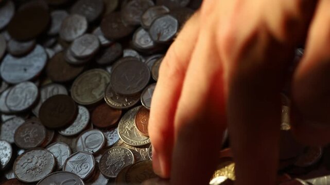 Old coins from different countries. Different currencies. Pile of old change in a box, unorganized coin collection. Hand grabbing and dropping coins, money
