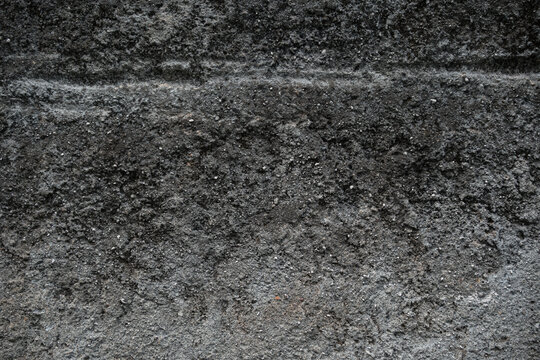 Dark grey rough asphalt texture. Gritty concrete surface background. Close up of grainy road or wall material.