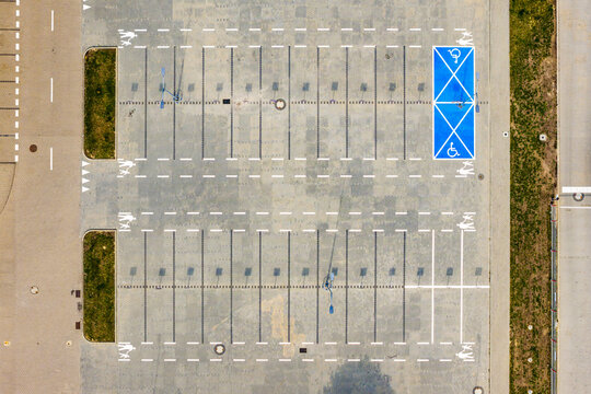 Aerial view of a parking lot with marked parking spaces, a blue-painted accessible parking spot, pedestrian crossings, and green patches in Warsaw, Masovian Voivodeship, Poland.