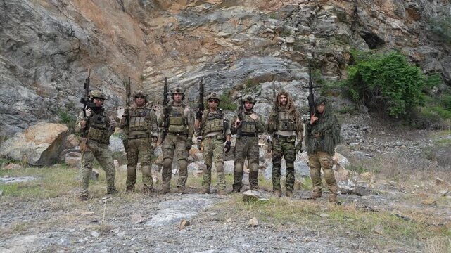 Multinational teams in military uniforms stand coolly, holding paintball guns, practicing combat techniques with explosion effects in the background of a mountainous jungle.
