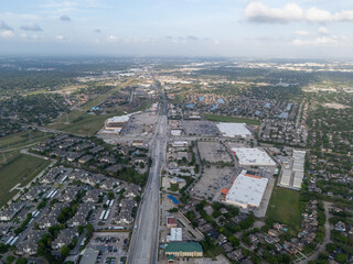 Fototapeta premium An aerial drone shot looking down a major road in a suburban area, featuring large retail shopping centers, parking lots, and surrounding residential housing developments in Houston, Texas