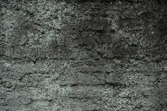 Dark grey rough concrete wall texture with a highly pitted and granular surface for industrial backgrounds.