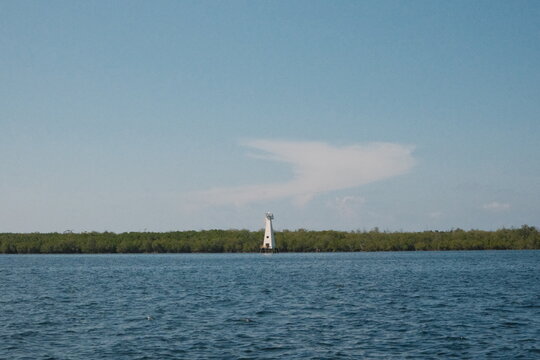 BERAS BASAH ISLAND, BONTANG, INDONESIA - JUNE 28, 2026: A distant lighthouse stands along the coastline of Beras Basah Island, framed by calm sea and clear blue skies in East Kalimantan.