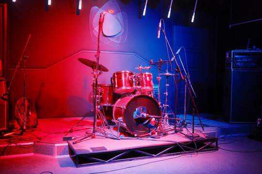 A drum set stands ready on a small stage in a music venue.