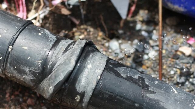 Close-up of leaking underground water pipe during repair work at an excavation site. Damaged pipeline with water escaping highlights plumbing maintenance, infrastructure failure, utility repair, and e