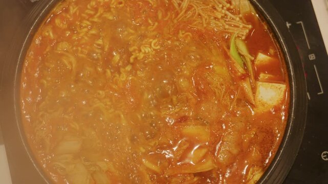 4K Slow motion Close-up top view of Korean army stew or Budae Jjigae bubbling and boiling with instant noodles, sausages and melted cheese in hot pot