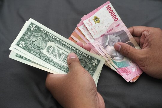 Close-up of hands holding United States dollar bills and Indonesian rupiah banknotes, showing currency exchange, finance, and money comparison.