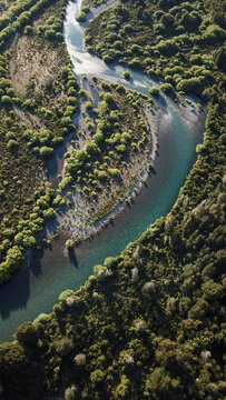 Aerial view of a winding river flowing through a dense forest with lush green trees and rocky banks in San Carlos de Bariloche, Rio Negro Province, Argentina.