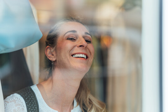 Beautiful blonde woman in authentic Bavarian dirndl gazing through the display window of a traditional clothing boutique in Bavaria.