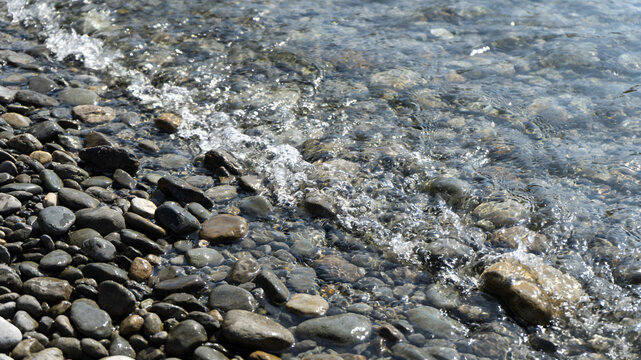 Clear water flowing over smooth river pebbles on sunny day
