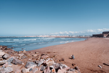 Obraz premium Vast sandy shoreline extending alongside a calm blue ocean, under a clear expansive sky. Scenic Coastal View with Sandy Beach and Blue Sky Horizon