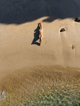 Aerial view of a woman in a bikini sunbathing on the sand at Little Boat Harbour Beach with clear turquoise water and long shadows in Bremer Bay, Western Australia, Australia.