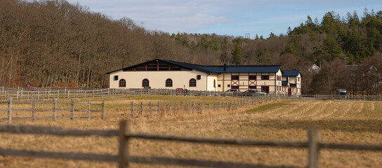 Fototapeta premium Large equestrian stable building beyond fenced fields in rural countryside.