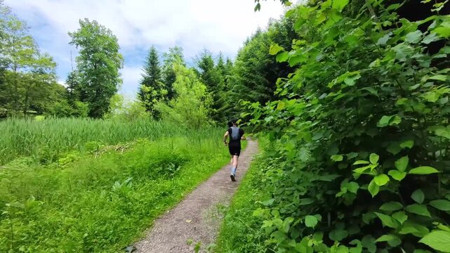 A solo trail runner follows a natural forest trail beneath a green canopy in Switzerland. Peaceful outdoor scenery highlighting fitness, adventure, and the enjoyment of nature.