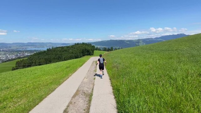 A trail runner follows natural paths through open meadows beneath a clear blue sky with views of Rigi and the Central Swiss mountains. Enjoying solitude, nature, and outdoor adventure in Switzerland.