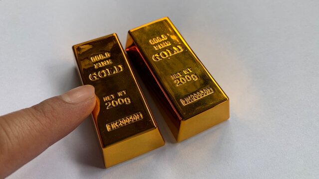 Two gold bars placed side by side with finger pointing, highlighting engraved &ldquo;fine gold&rdquo; text and comparable size