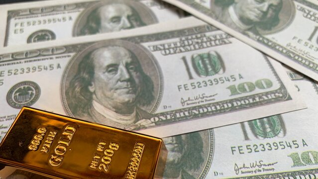 Gold bar placed over American hundred dollar banknotes, symbolizing stable asset allocation and financial security strategies
