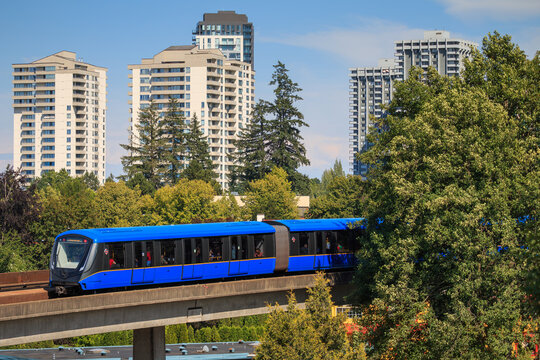 Skytrain travels through Vancouver's urban area with buildings and trees in the background on a clear day