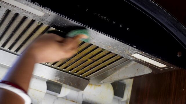 Woman hand cleaning or servicing cooker hood or kitchen chimney with green sponge in home kitchen. cleaning hygiene maintenance kitchen concept.