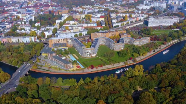 Aerial drone view of the Bundesschlange snake-shaped residential complex along the Spree River with tour boats and autumn trees in Moabit, Berlin, Germany.