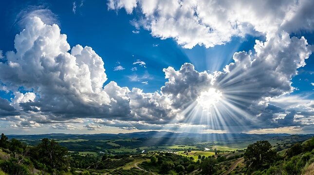 Dramatic cumulus clouds and sunburst over rolling hills landscape