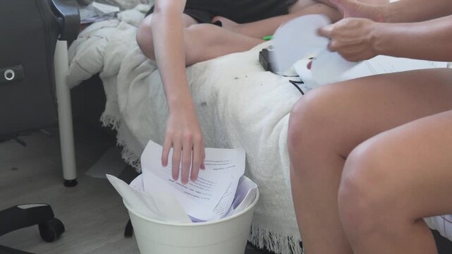 Teenager throwing old school papers into a trash bin while sorting documents at home. Student decluttering study materials after school, cleaning a messy bedroom and organizing paperwork
