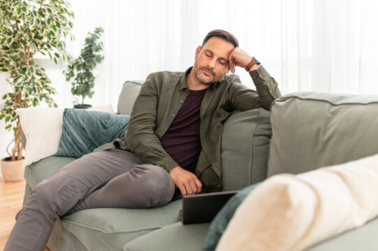 Man resting on a couch at home, experiencing fatigue and mental exhaustion, taking a brief pause from work, needing a moment of relaxation and self care