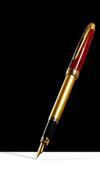 A fountain pen is positioned above a blank piece of paper. The pen has a golden body with a red section. The background is dark, creating contrast with the pen and paper.