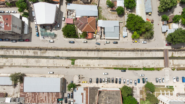 Aerial view of a town street with a canal running through the center, lined with parked cars, buildings, and green trees in Provadia, Varna, Bulgaria.