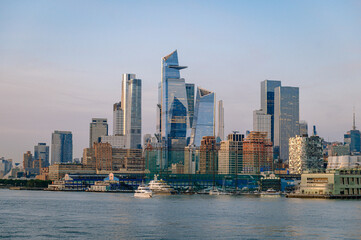 Obraz premium Hudson Yards and Chelsea Piers from the Hudson river at sunset, New York. Wide view of modern glass towers, yacht marina, Marine Aviation pier and pale blue sky.