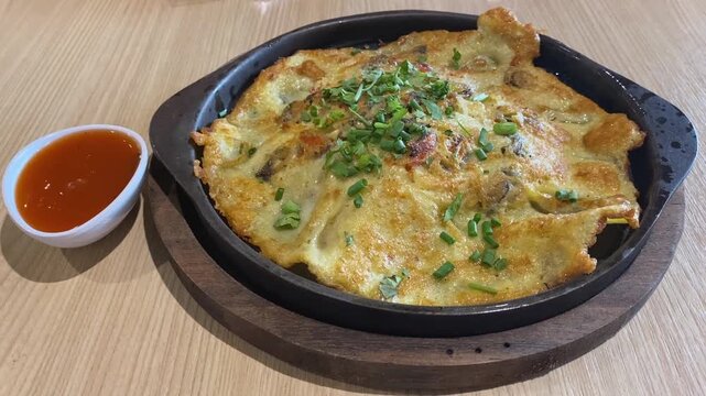 Traditional Thai Crispy Fried Clam Mussel Seafood Omelette Pancake (Hoy Tod) with Red Chili Dipping Sauce In Cast Iron Skillet Served Cooked in Bangkok Street Food Restaurant
