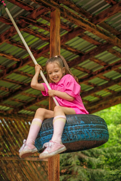 A happy, laughing girl is swinging on a suspended wheel tire. Children's entertainment