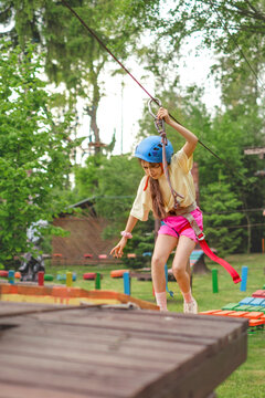 A child wearing protective sports gear is running, stumbling, and falling on a suspended bridge in an outdoor adventure park.