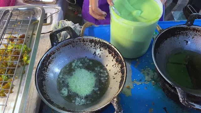 Deep Fried Thai Pandan Green Coconut Rice Flour Pancake Dessert (Kanom Fak Bua) in Hot Oil Wok.  Vendor Cooks Authentic Thailand Street Food at Bangkok Open Market