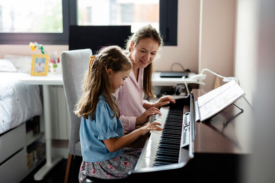 Woman helping girl learning piano at home