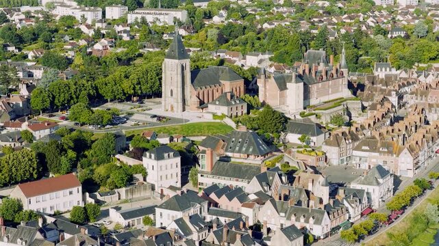 A high-resolution aerial video captures the picturesque town center of Gien, France, showcasing its iconic church, historic chateau, and charming old town architecture surrounded by lush greenery