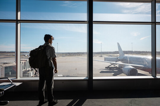 Man looking at airplane from airport terminal window