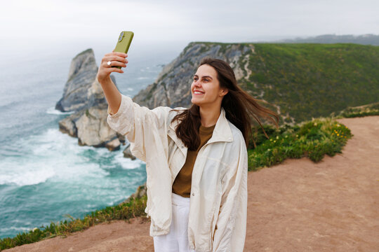 Woman taking selfie with smartphone at Cabo da Roca cliffs