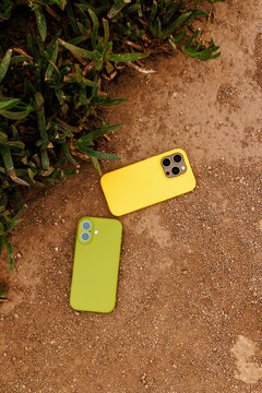 Two smartphones with colored cases on dirt ground