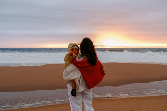 Mom holding child on beach at sunset