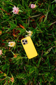 Yellow smartphone on green grass with flowers outdoors