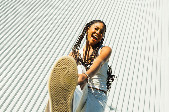Young woman posing playfully with sneakers toward camera in urban sett