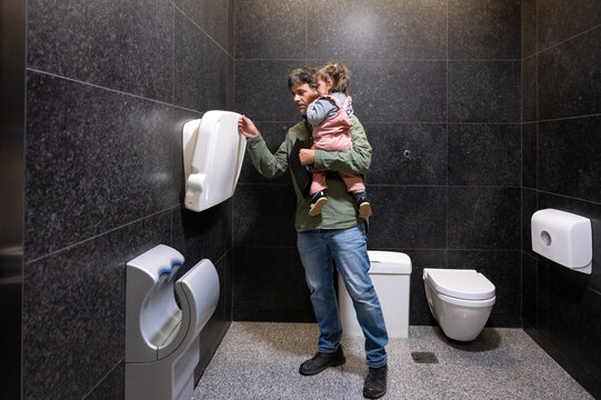Father Carrying Toddler After Diaper Change In Public Bathroom