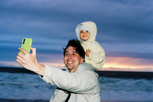 Man using smartphone take selfie with child at beach film photo