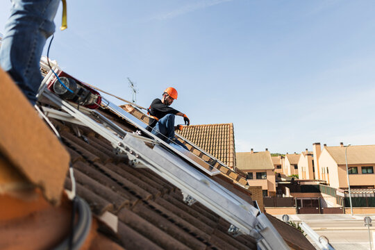 Worker installing solar panels on tiled building roof