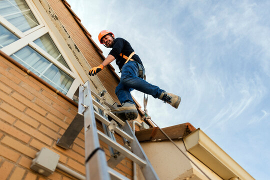 Builder climbing ladder wearing safety equipment smiling