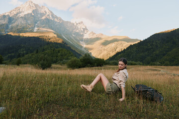 Obraz premium Woman traveler relaxing in a meadow with distant mountains, wearing hiking clothes, sunlit outdoor scene, capturing a calm nature lifestyle moment in landscape