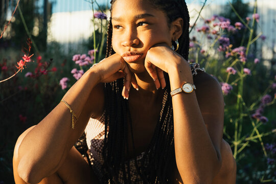 Thoughtful young woman surrounded by flowers in warm sunlight